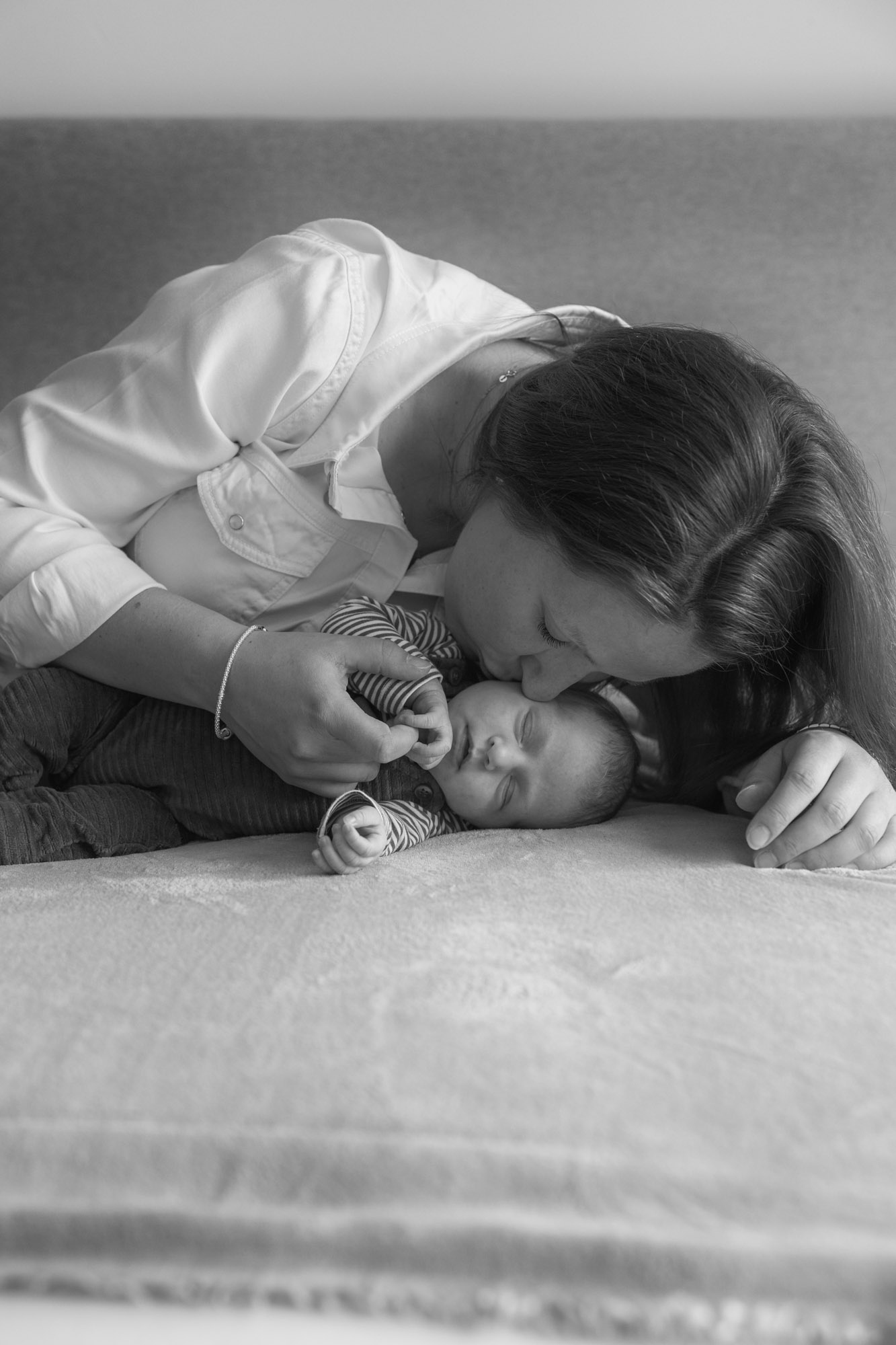 Moeder en newborn knuffelend op ouderlijk bed door Mayra Fotografie